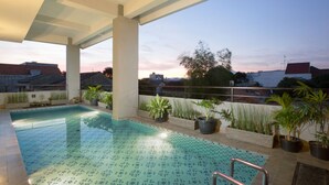 Una piscina interior con suelo de baldosas, rodeada de plantas en macetas y un área cubierta con columnas.