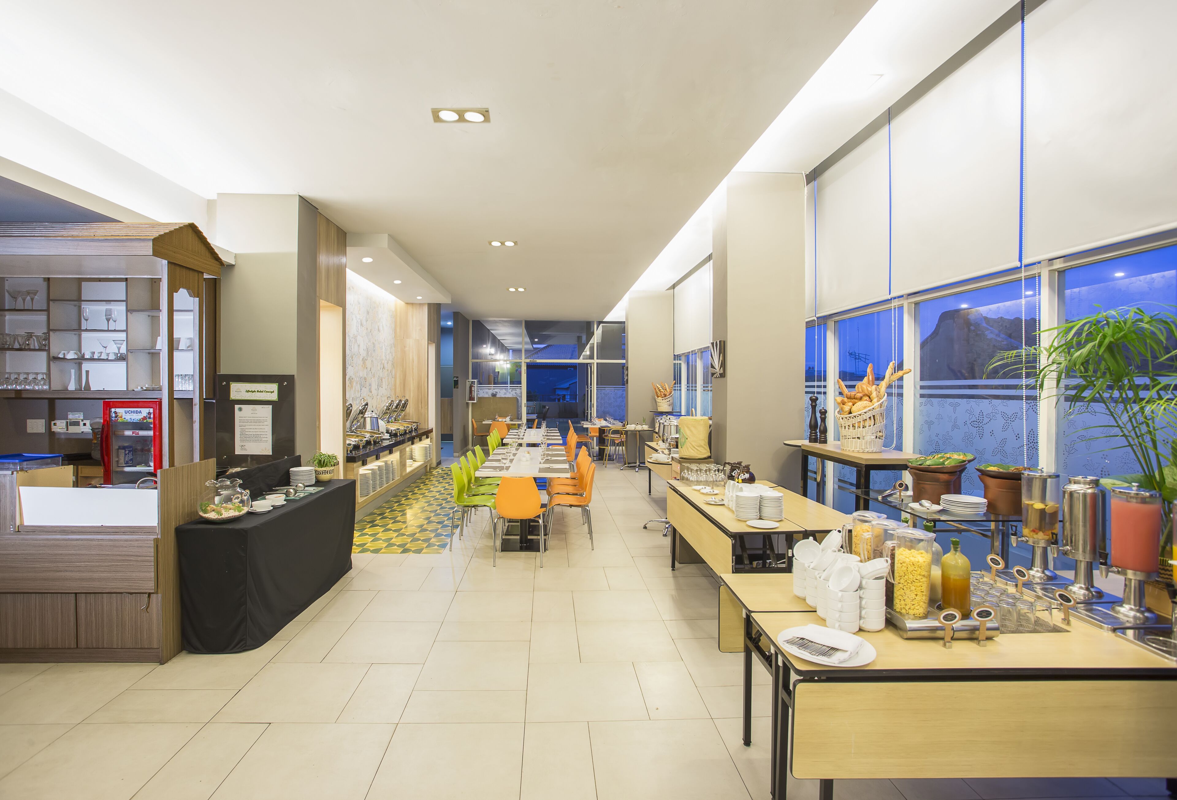 A modern dining area with a long counter, orange chairs, and various food and drink stations.