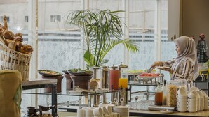 Un bufé de desayuno con diferentes alimentos, una planta y una persona atendiendo.