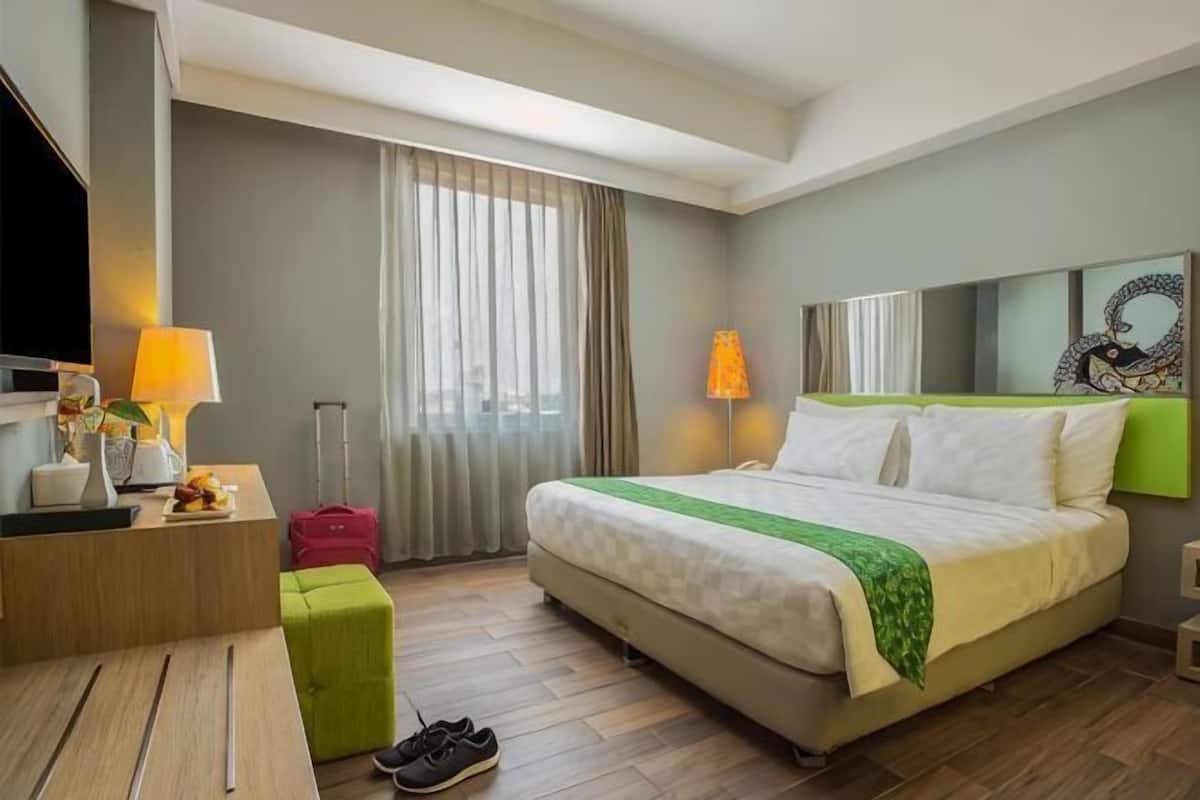A hotel room with a bed, a desk, a television, a lamp, a suitcase, and a window with curtains.