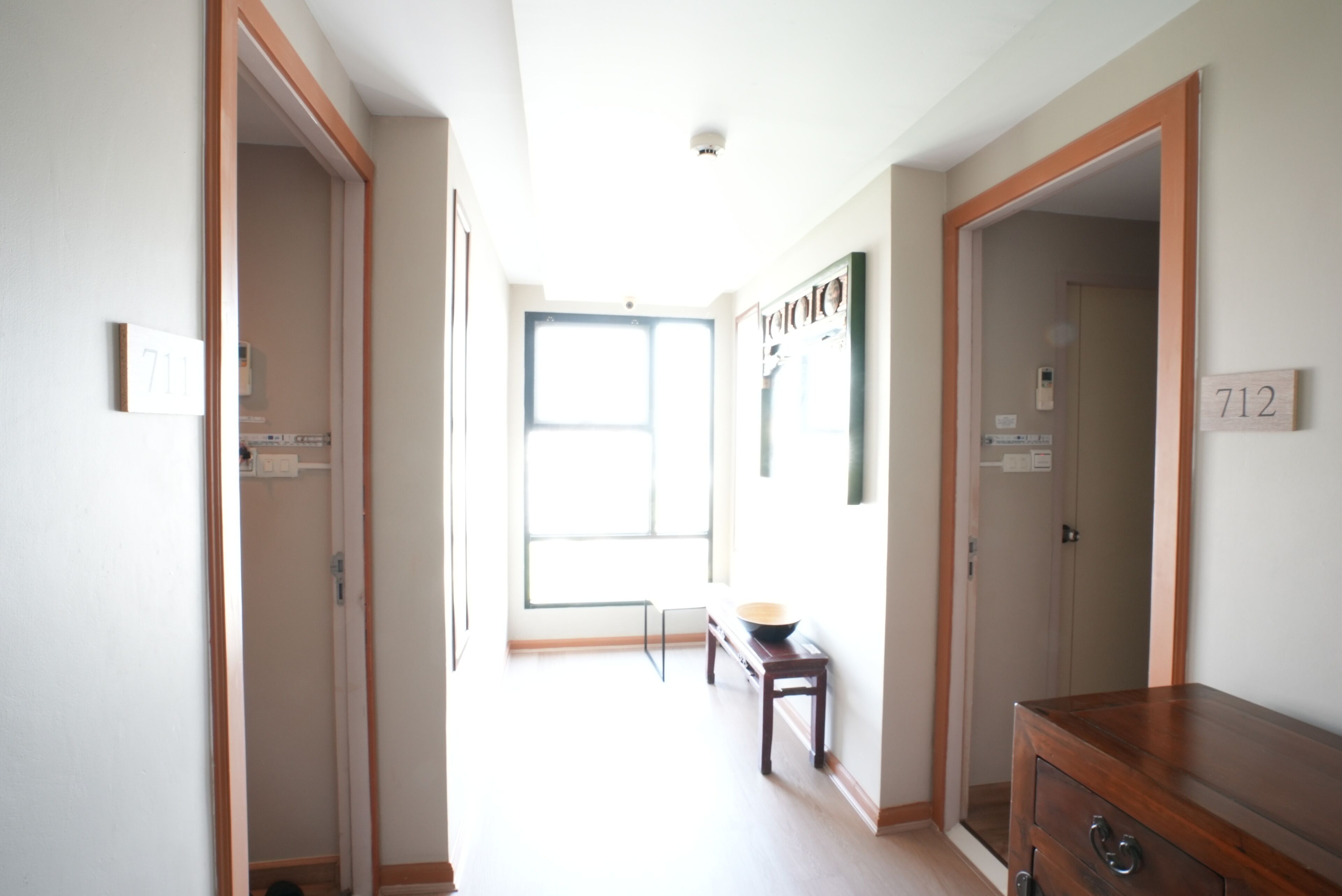 Un couloir avec des portes en bois, des panneaux indiquant les numéros des pièces et une petite table sur laquelle se trouve un bol.