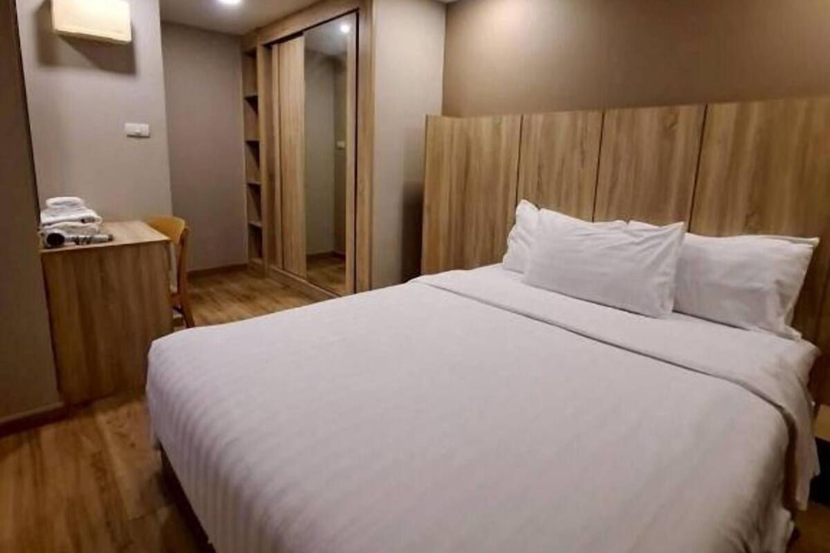 A hotel room with a large bed, wooden headboard, and a small desk with a chair.