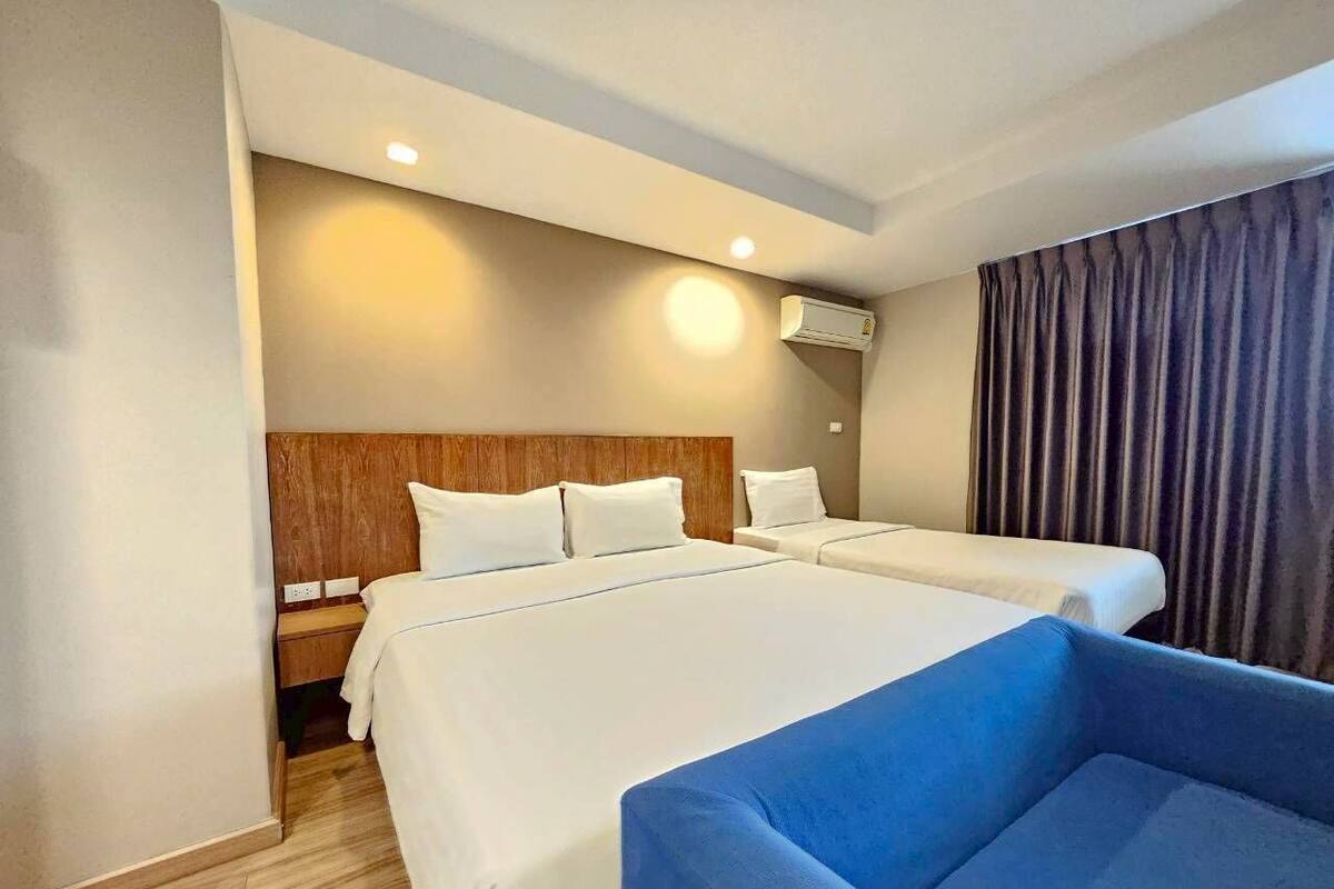 A hotel room with two beds, a blue chair, a wooden headboard, a nightstand, and an air conditioning unit.