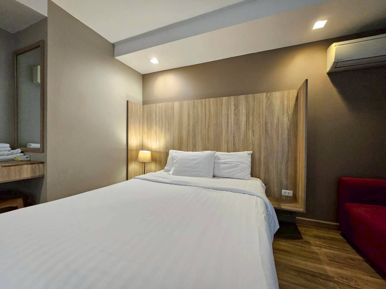 Una habitación de hotel con una cama grande, un cabecero de madera, una mesita de noche con una lámpara y una silla roja.