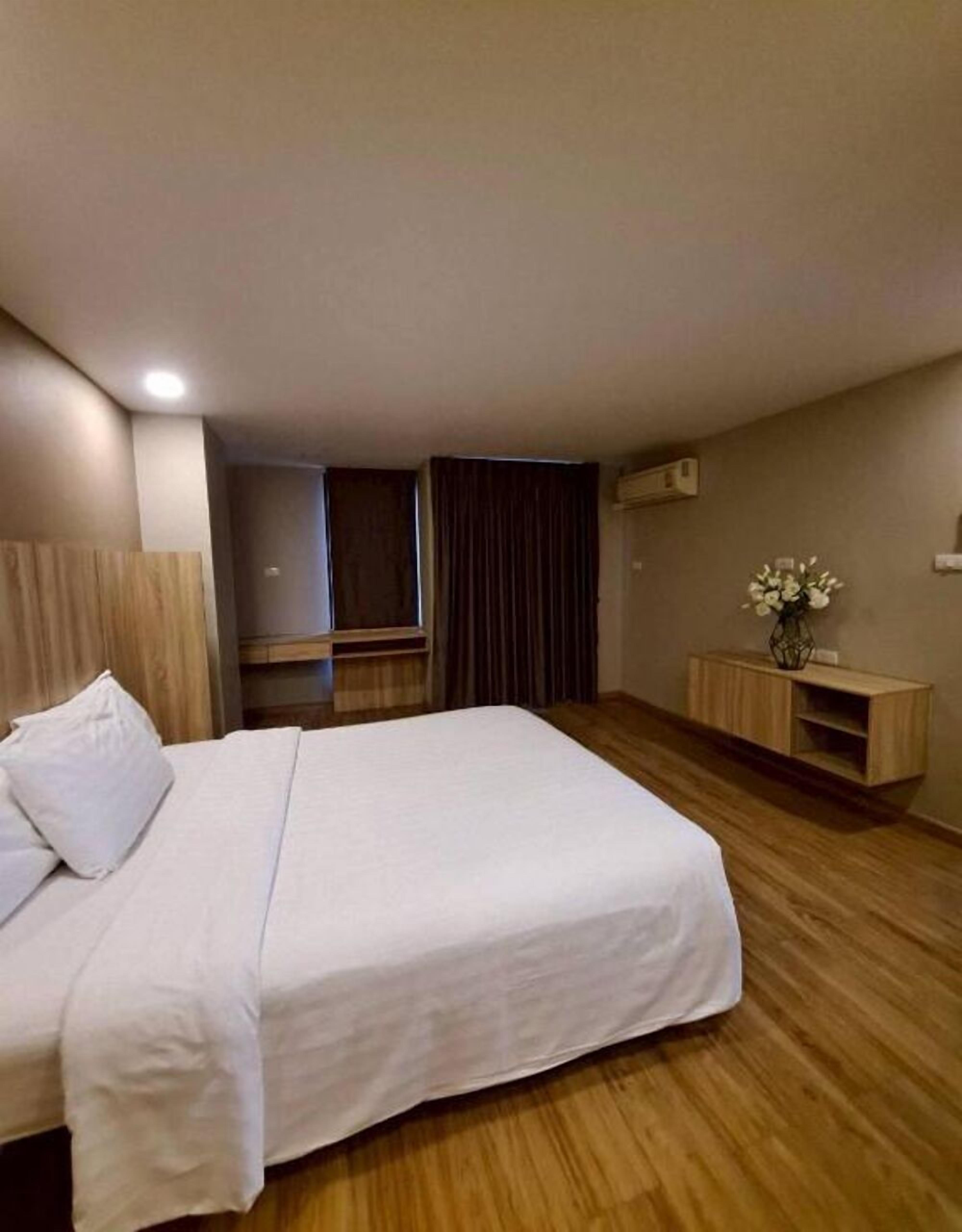 Ein Hotelzimmer mit einem großen Bett, Holzboden, einem kleinen Schrank und einem Fenster mit Vorhängen.
