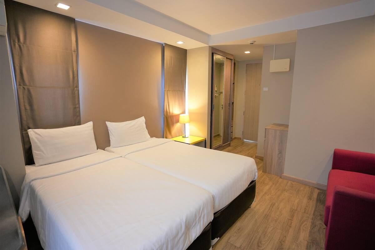 A hotel room with a double bed, a bedside table with a lamp, a red chair, and a wardrobe.