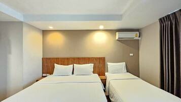 Habitación de hotel con dos camas, cabecera de madera, unidad de aire acondicionado y una cortina a la derecha.