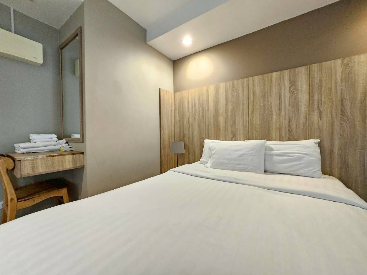 A hotel room with a bed, a desk with a chair, a lamp, and a mirror.