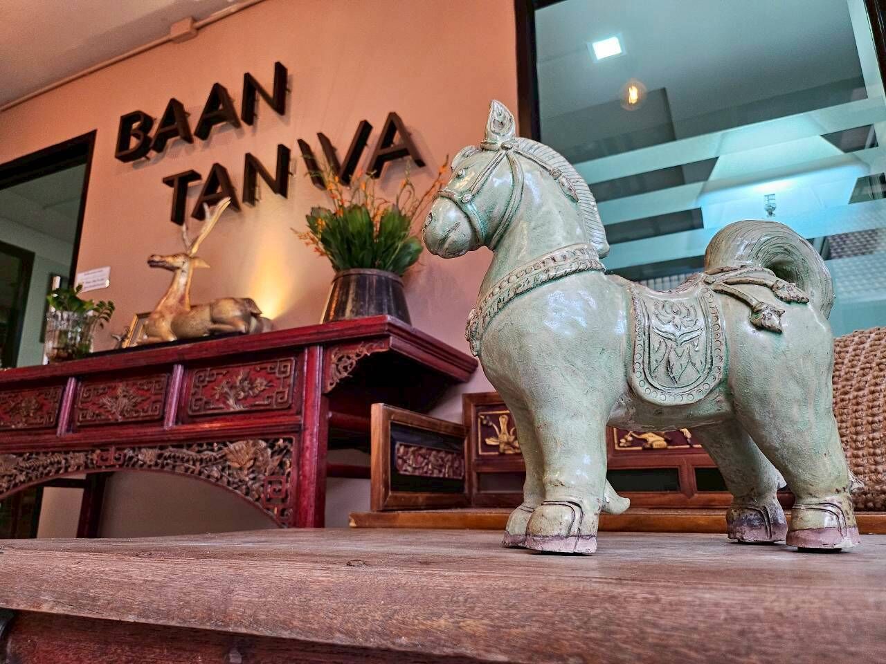 A decorative horse statue on a wooden table in a room with a sign reading "BAAN TANIVA".