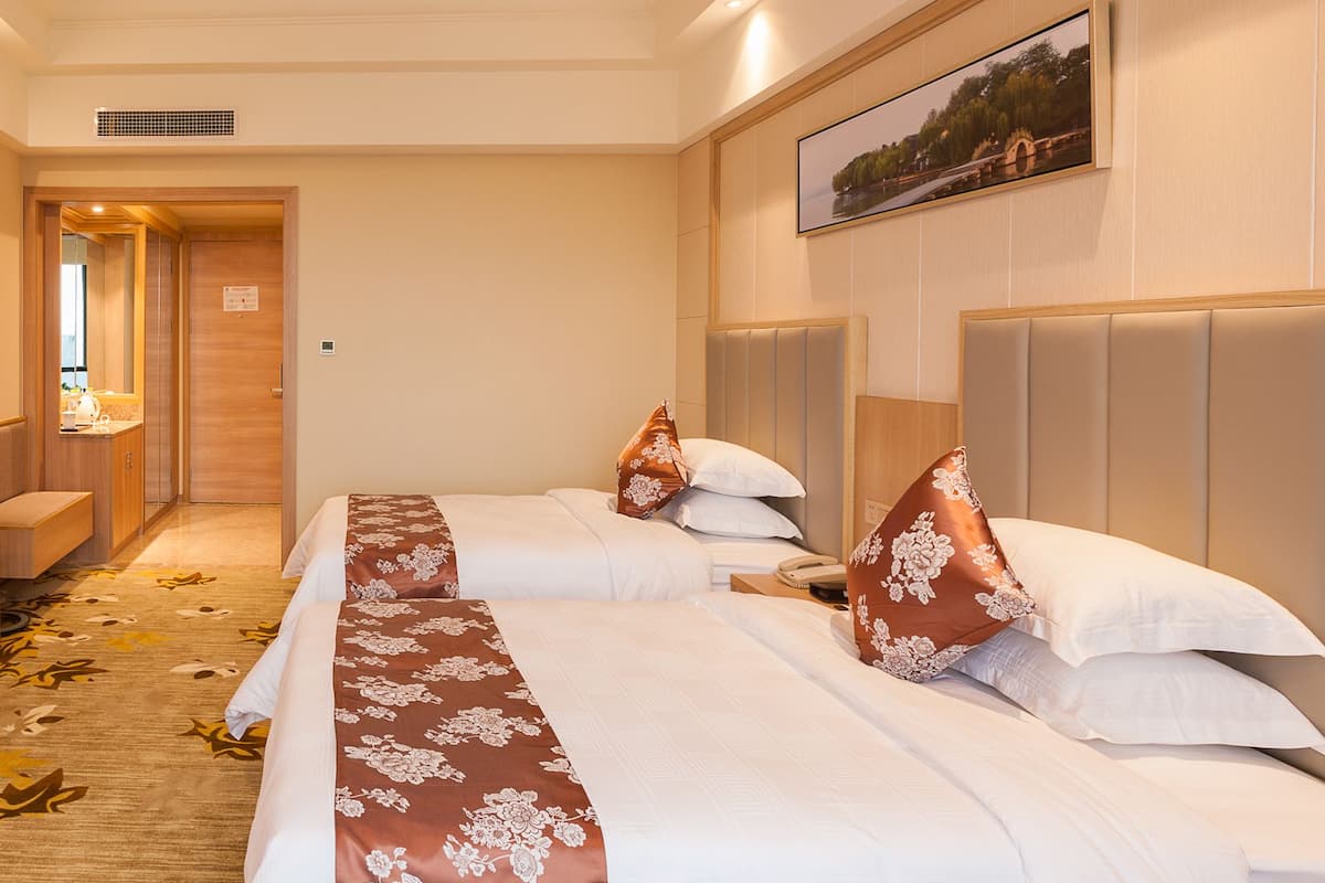 Une chambre d’hôtel avec deux lits, un plancher en bois, un tableau au mur et une porte donnant sur une autre pièce.