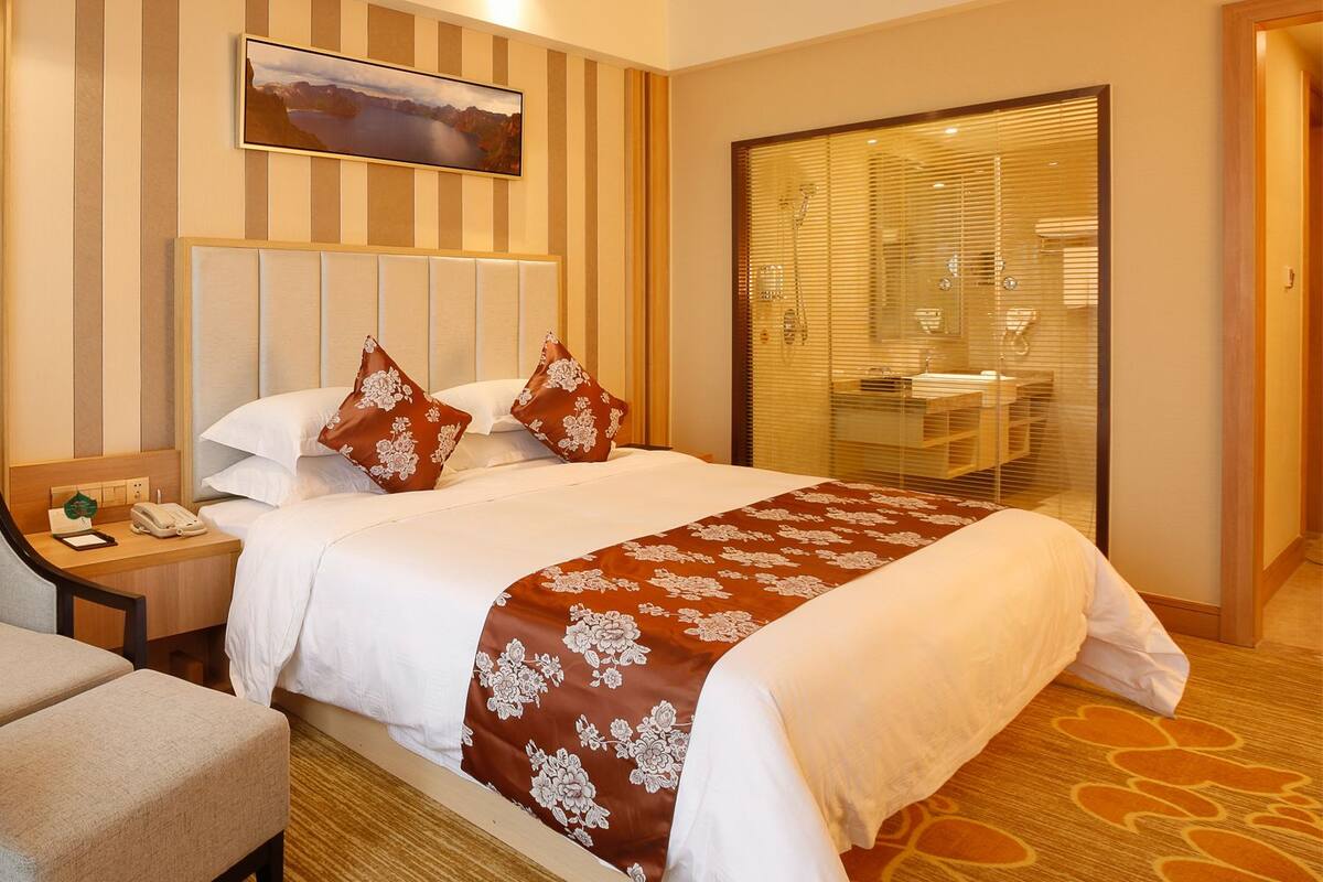 Une chambre d’hôtel comprenant un lit, un bureau, une chaise, une salle de bain avec douche et un tableau au mur.