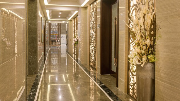 A hotel corridor with a polished marble floor, decorative panels, and a floral arrangement. - Hangzhou OUYAMEI International Hotel (Hangzhou)