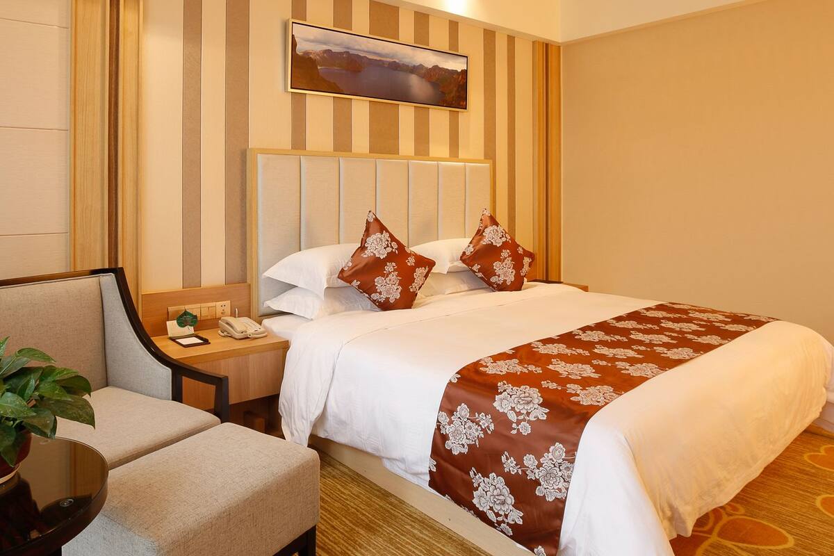 Une chambre d’hôtel avec un lit, une table de chevet avec un téléphone, une chaise et une plante.