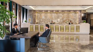 A reception area with a marble reception desk, a seating area with chairs, and a decorative wall with geometric patterns. - Hangzhou OUYAMEI International Hotel (Hangzhou)