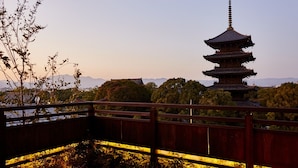 Un pagode japonés tradicional con varios niveles, rodeado de exuberante vegetación y una cerca de madera.