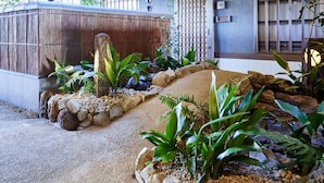 Un jardín japonés tradicional con un sendero de piedra, una valla de bambú y diversas plantas.