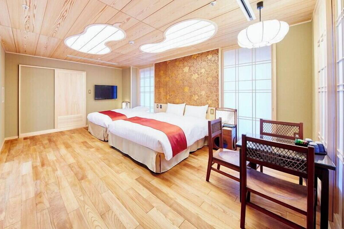 A bedroom with a wooden floor, a bed with a red and white bedspread, a wooden chair, and a TV mounted on the wall.