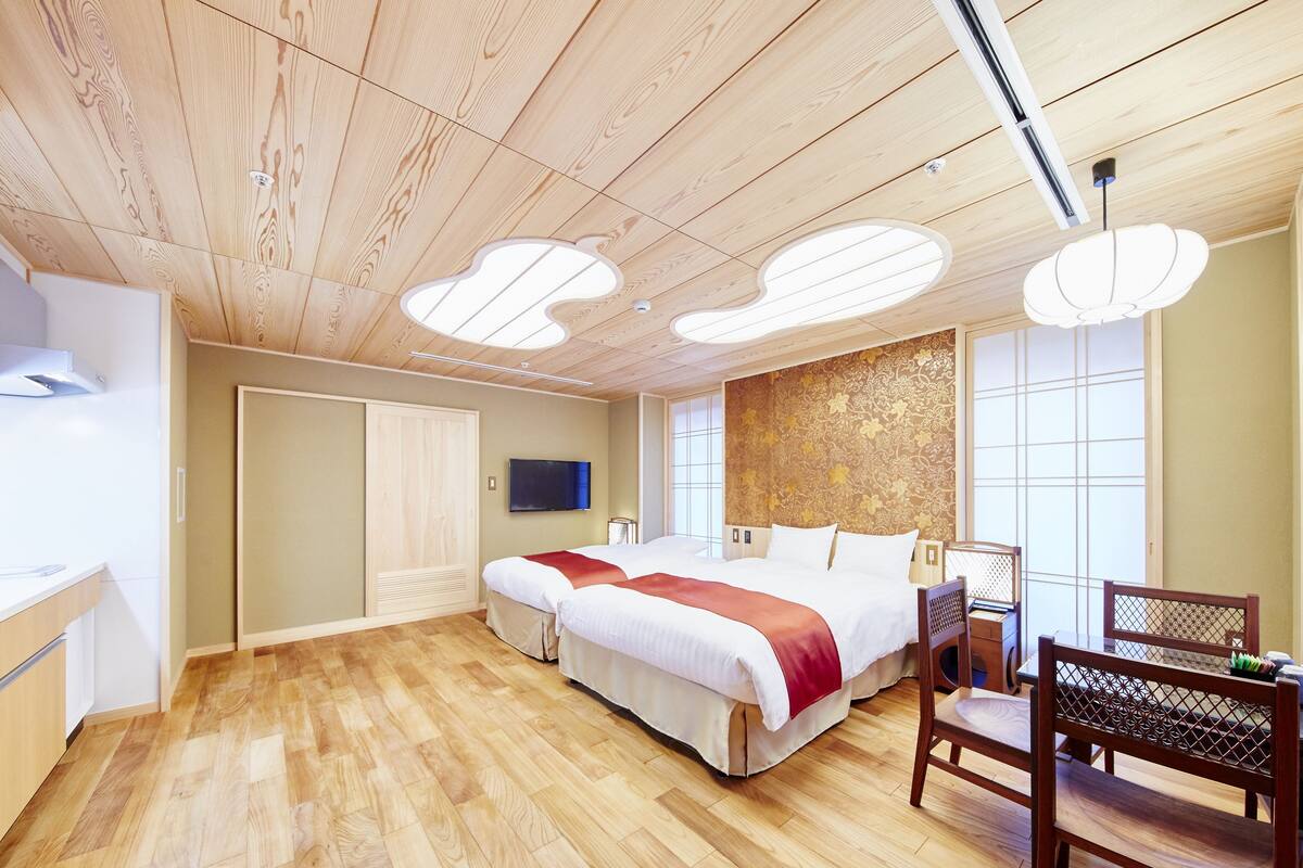 A hotel room with a wooden ceiling, a bed with a red blanket, a TV, a nightstand, and a chair.