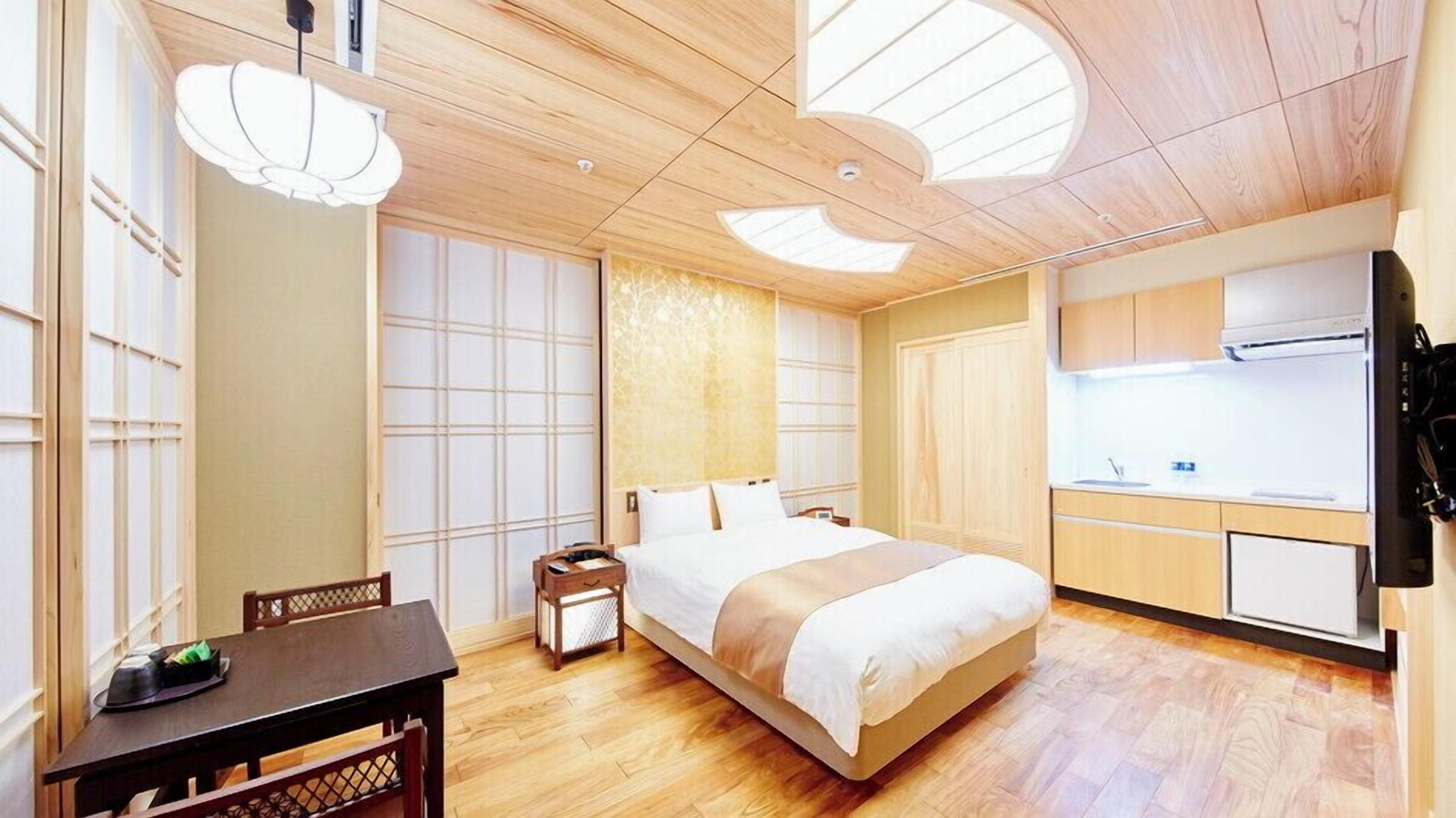 A hotel room with a bed, a dining table, a small kitchen area, and a large window with a view.