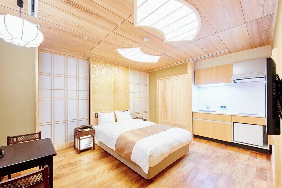 A hotel room with a bed, a dining table, a small kitchen area, and a large window with a view.