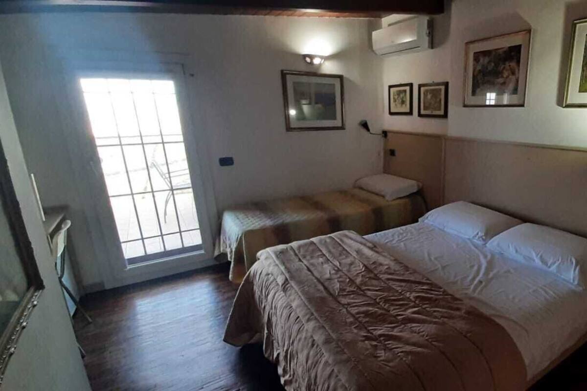 A room with two beds, a radiator, and framed pictures on the wall.