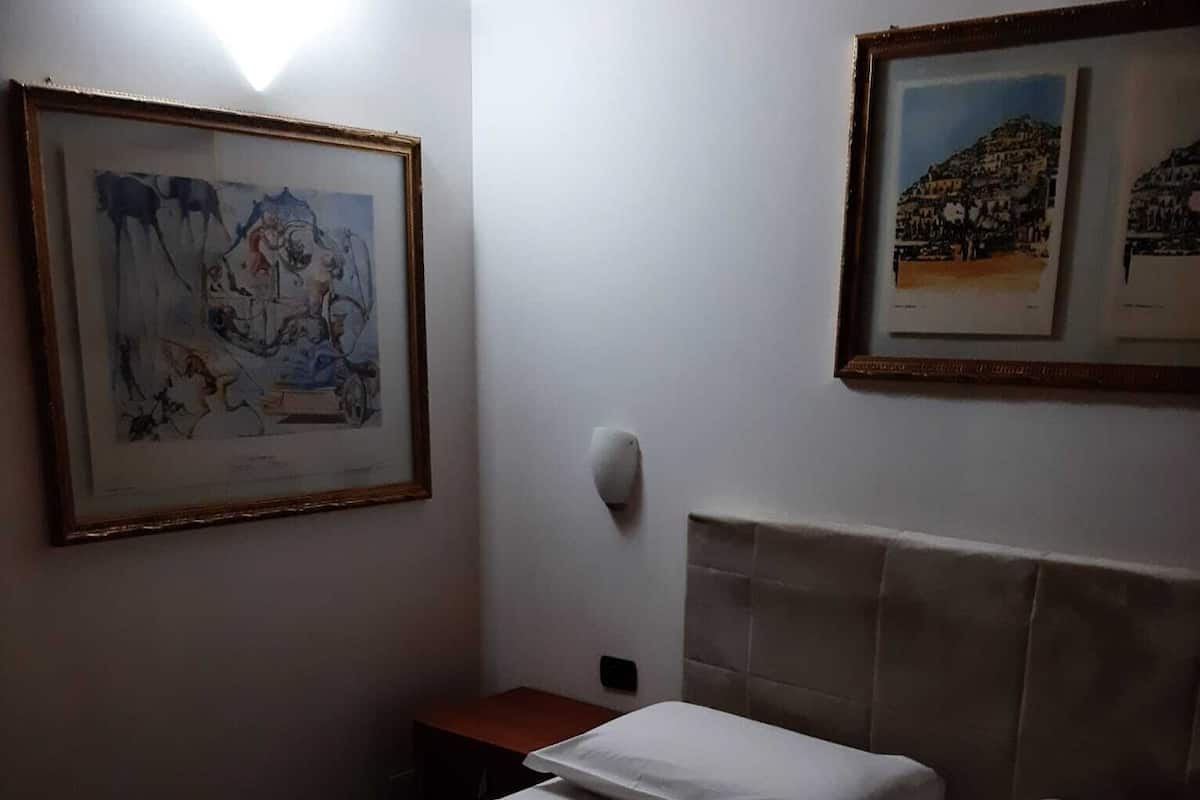A hotel room with a bed, a nightstand, and two framed pictures on the wall.