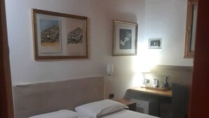 Ett sovrum med en säng, två inramade tavlor på väggen, ett skrivbord med en lampa och ett träpanelat tak.
