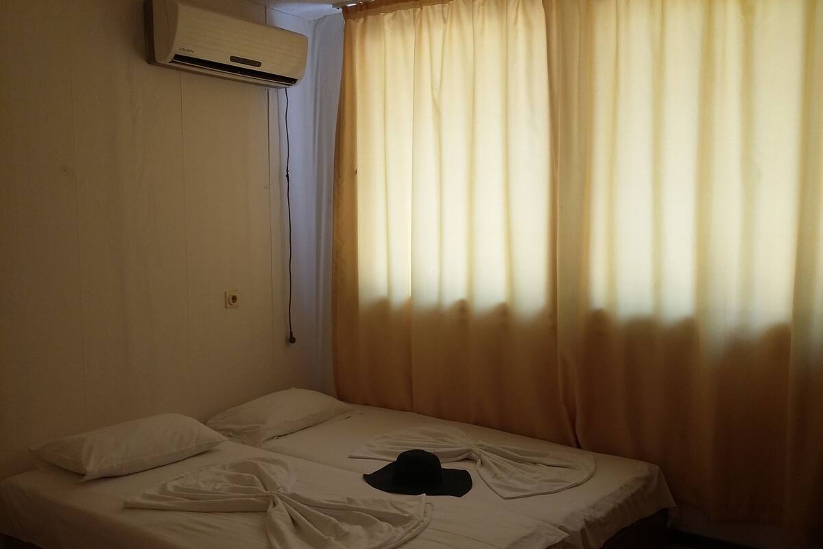 A single bed with white bedding, a black item on the bed, and a window with beige curtains.