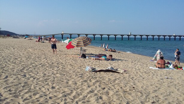 Ein sandiger Strand mit einem Pier im Hintergrund.