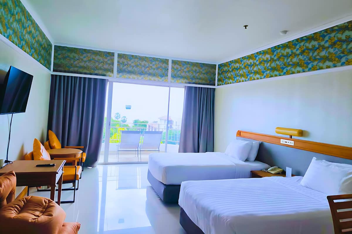 Une chambre d’hôtel avec deux lits, un bureau, une chaise, une télévision et un balcon avec des rideaux.