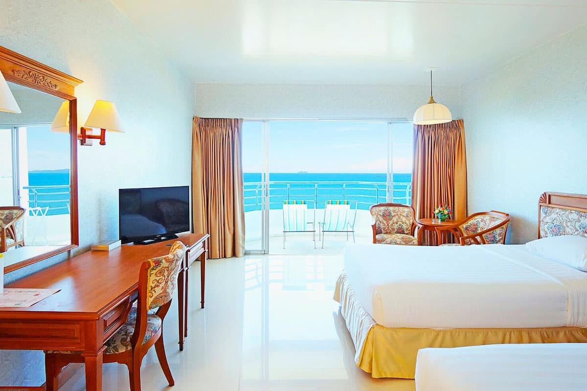 Une chambre d’hôtel équipée d’un lit, d’un bureau, d’une télévision et d’un balcon avec vue sur la mer.