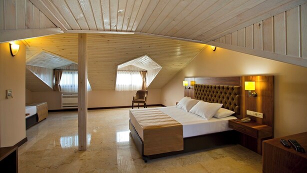 A spacious attic bedroom with a large bed, a chair, and a desk. - Hotel Montana (Ortaca)