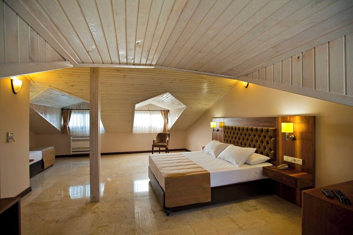 A spacious attic bedroom with a large bed, a chair, and a desk.