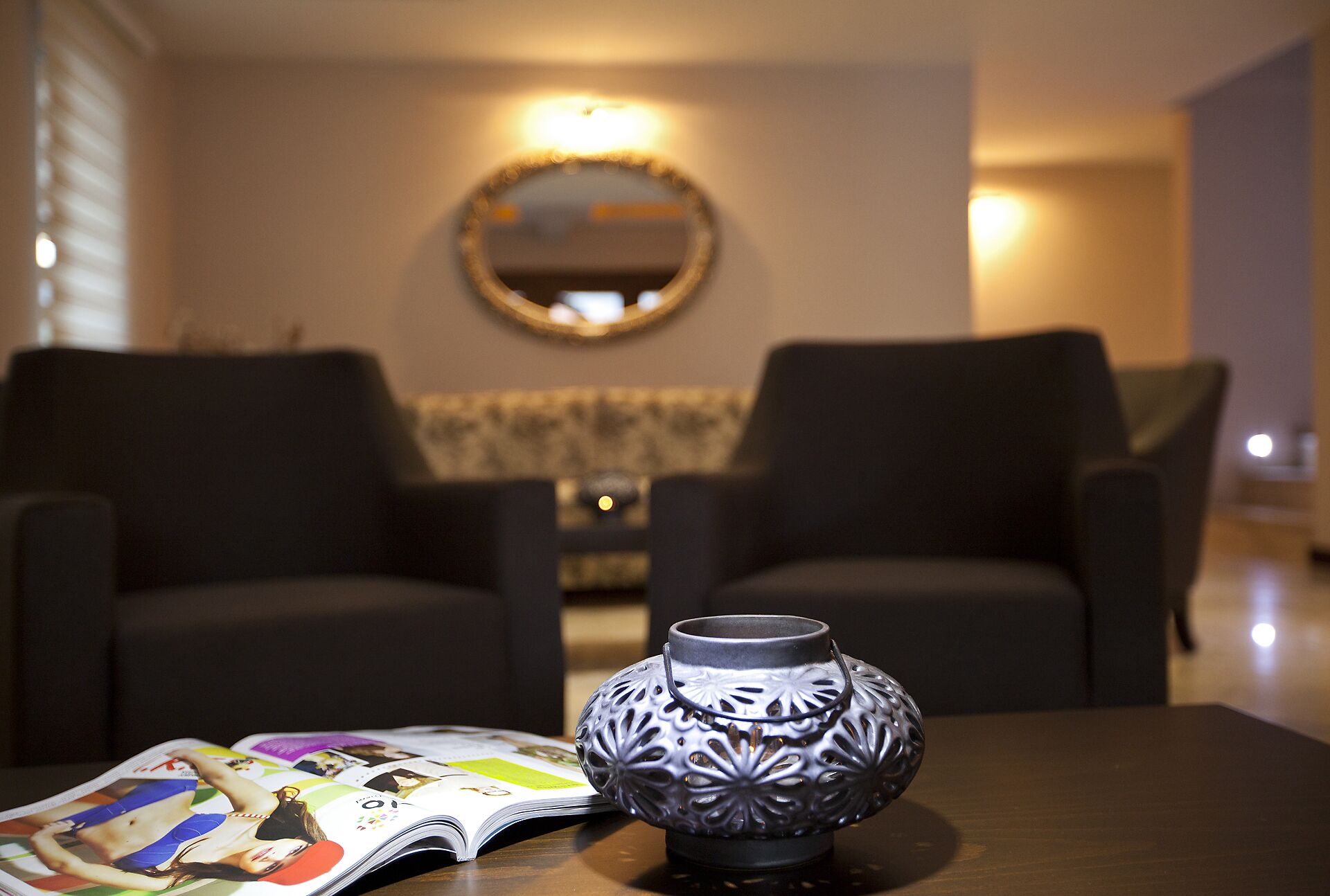 Una sala moderna con dos sillones oscuros, un florero decorativo y una revista sobre una mesa de madera.