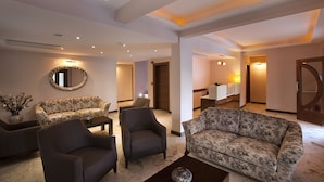 Amplia sala de estar con un sofá, sillones y una mesa de centro. Hay un espejo en la pared y una puerta que da a otra habitación.
