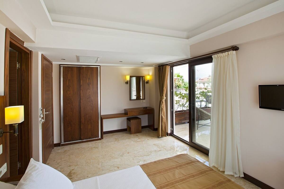 A hotel room with a bed, a desk, a mirror, a TV, and a sliding glass door to an outdoor area.