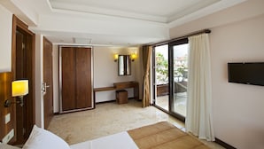 Habitación de hotel con cama, escritorio, espejo, televisión y puerta corredera de vidrio a un área exterior.