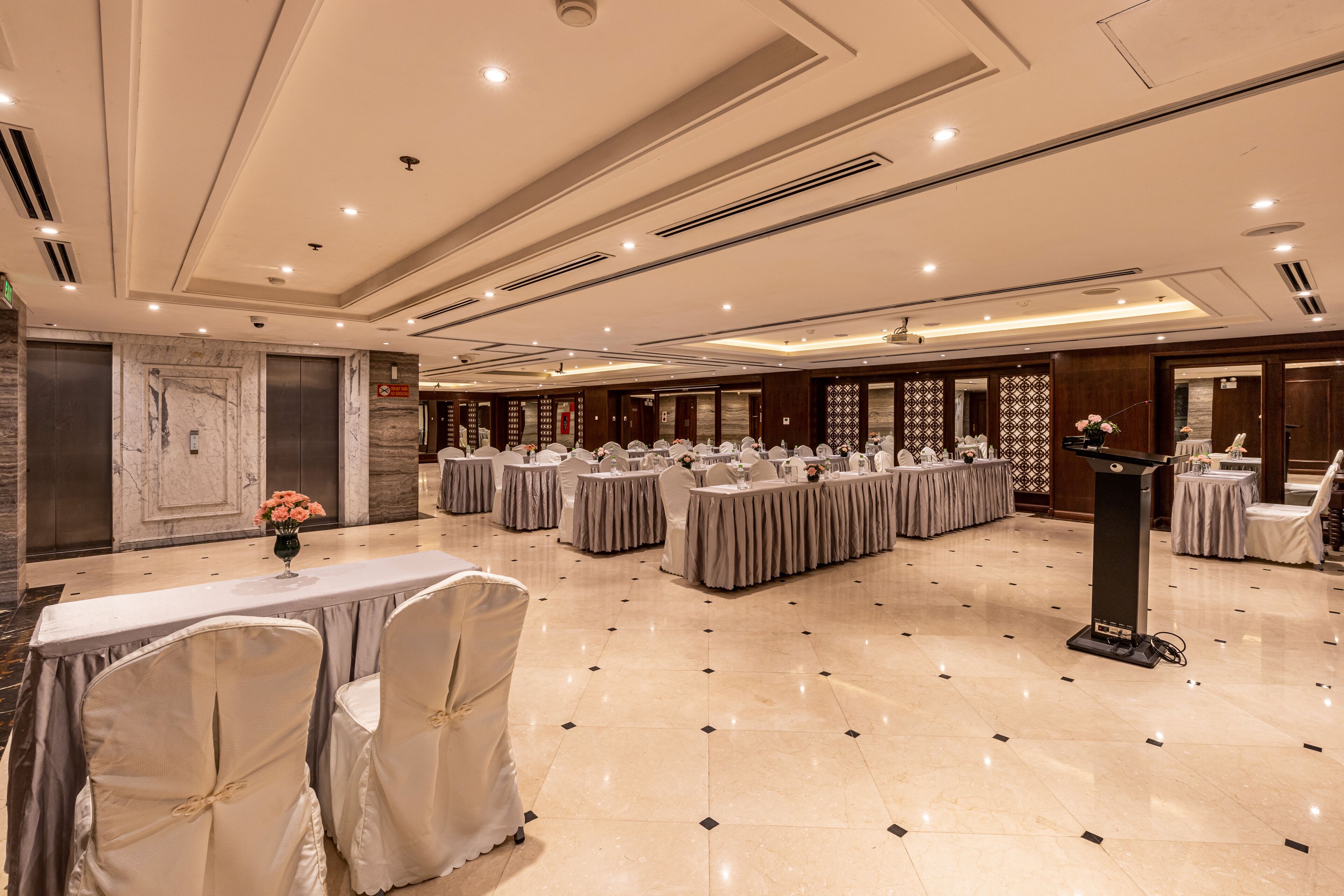 A spacious banquet hall with multiple round tables, chairs, and a podium.
