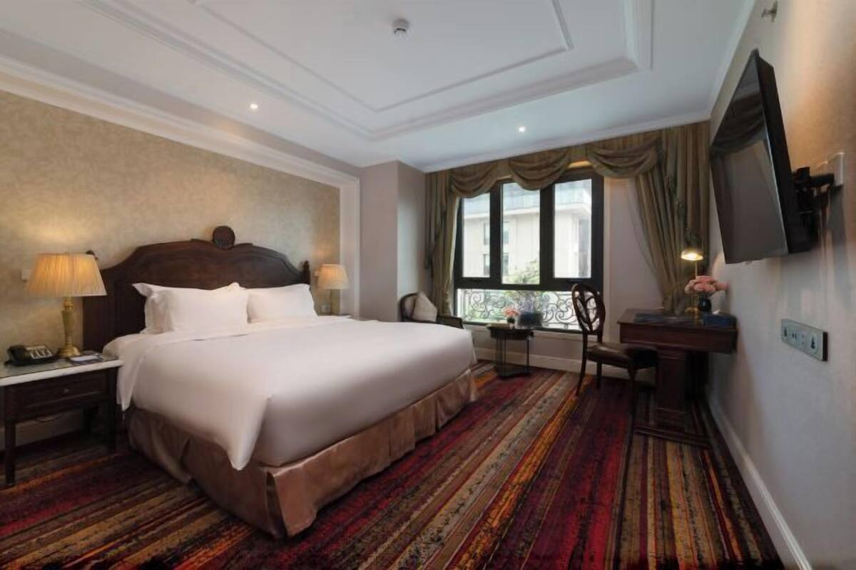A hotel room with a large bed, a desk, a chair, a TV, and a window with curtains.