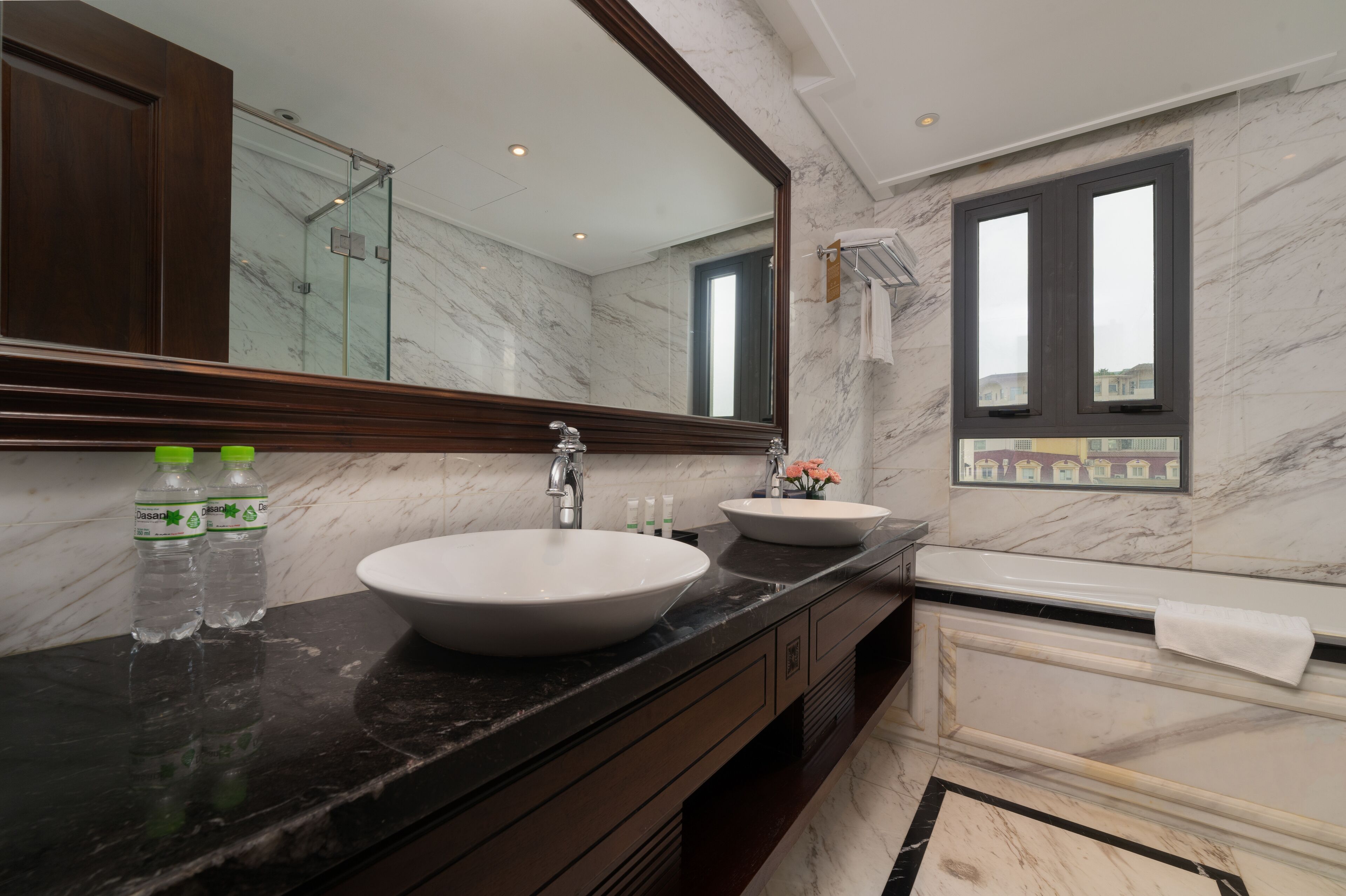 A modern bathroom with marble walls, two sinks, a large mirror, and a bathtub.