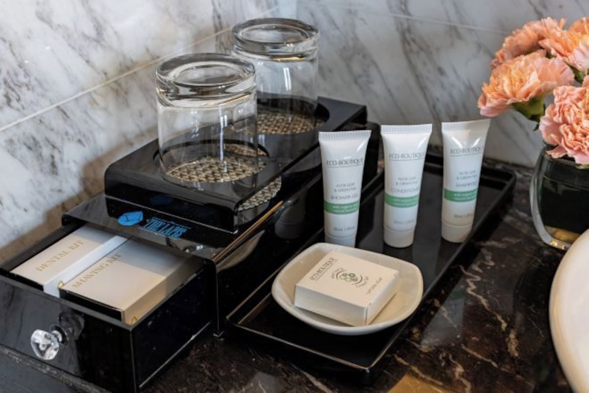 A bathroom vanity with a marble countertop, a black tray holding toiletries, and a vase with flowers.