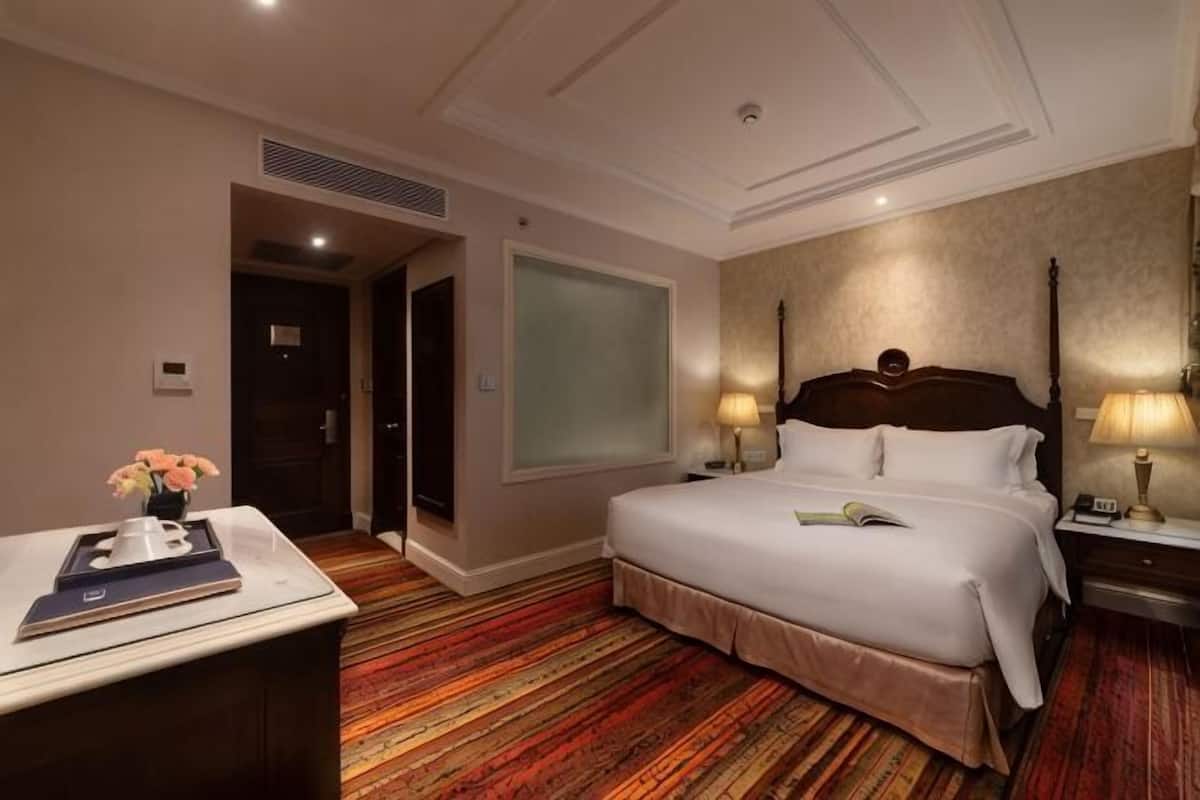 A hotel room with a large bed, bedside tables, a desk, and a window.