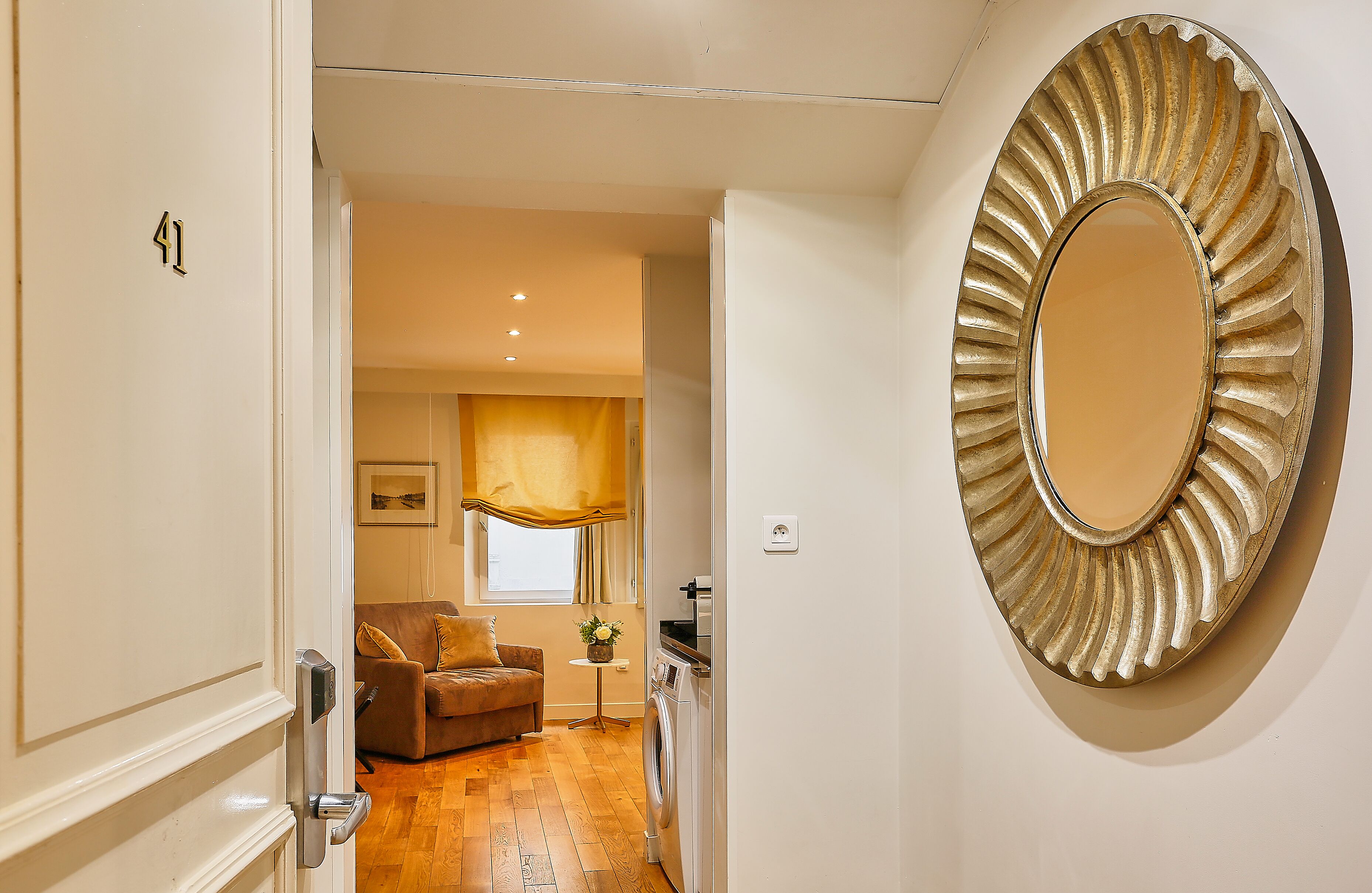 A hallway leading to a living area with a sofa, a small table, and a washing machine.