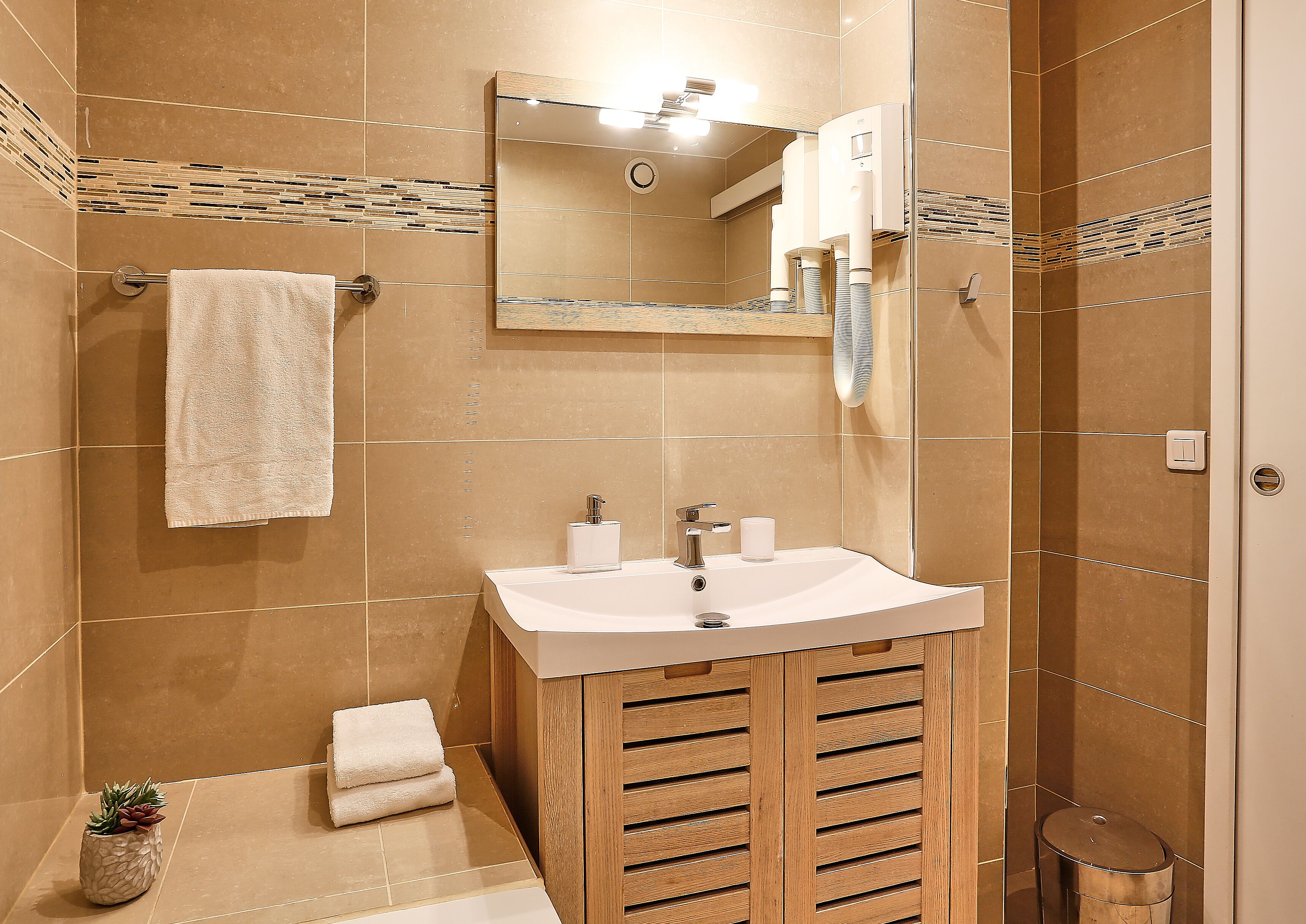 Ein modernes Badezimmer mit Waschbecken, Spiegel, Handtuchhalter und einer kleinen Mülltonne.