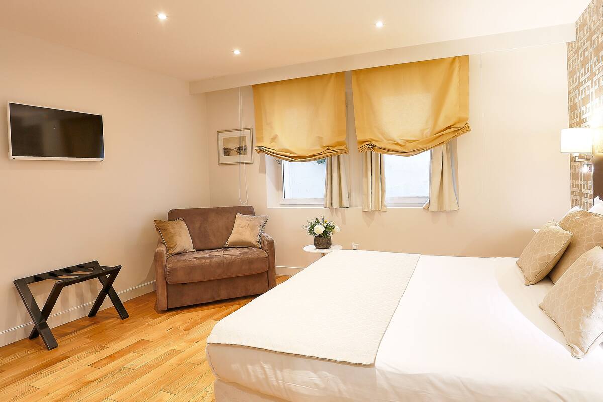 A hotel room with a large bed, a sofa, a TV, and a window with curtains.