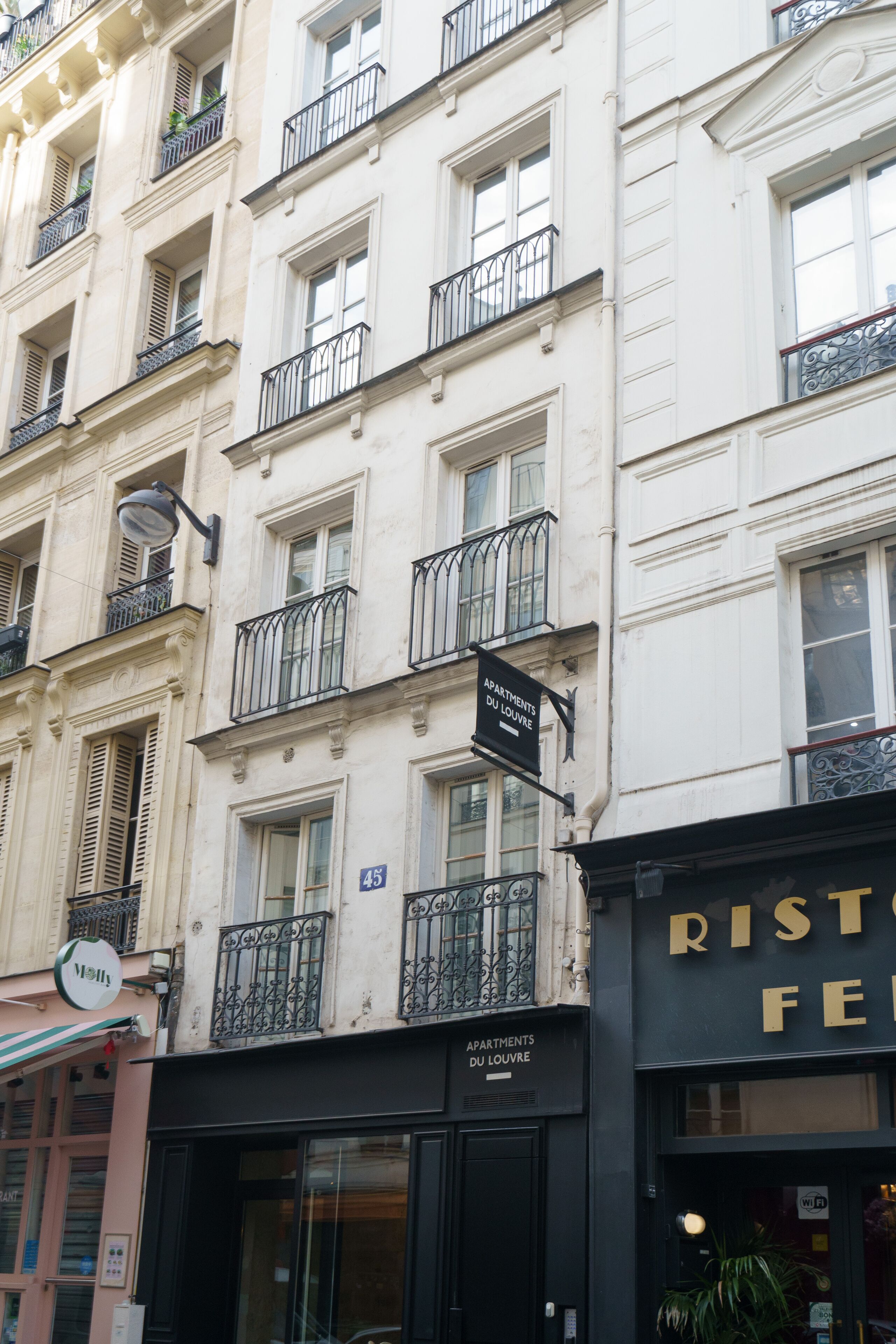 A multi-story building with balconies, a sign for 'Apartments du Louvre', and a restaurant named 'Risto'.