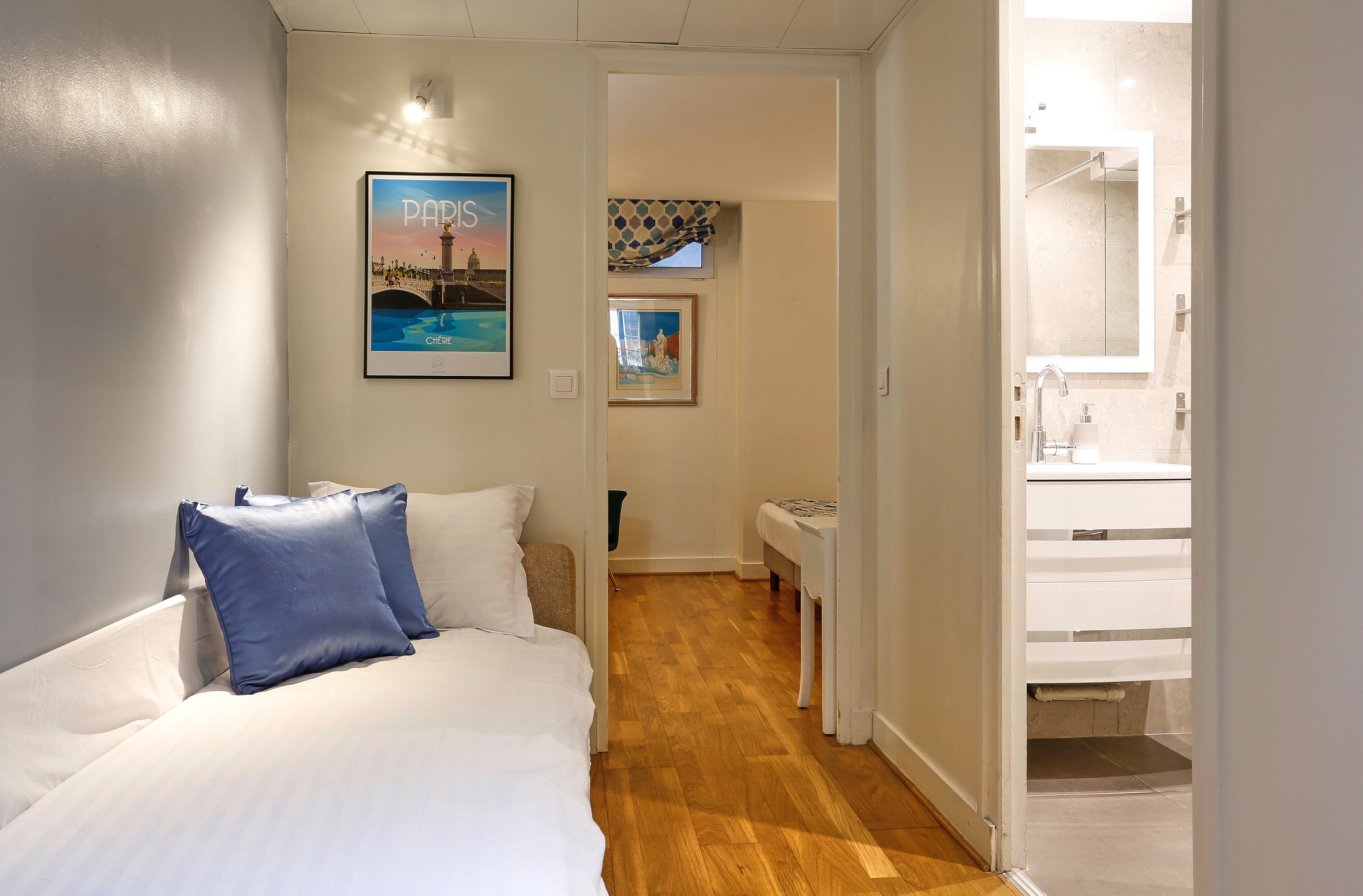 Quarto de hotel com cama, uma mesinha, espelho e banheiro visível através de uma porta aberta.