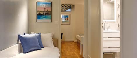 A hotel room with a bed, a small table, a mirror, and a bathroom visible through an open door.