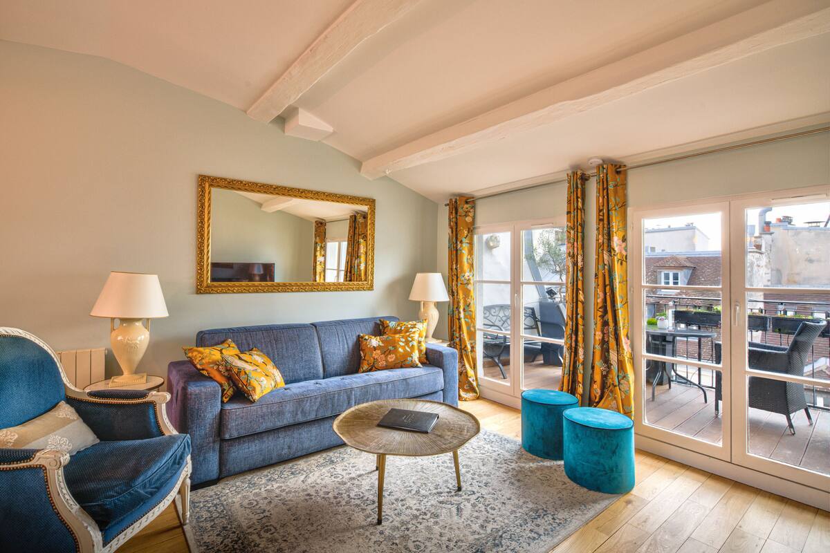 A living room with a blue sofa, a coffee table, and a large window with curtains.