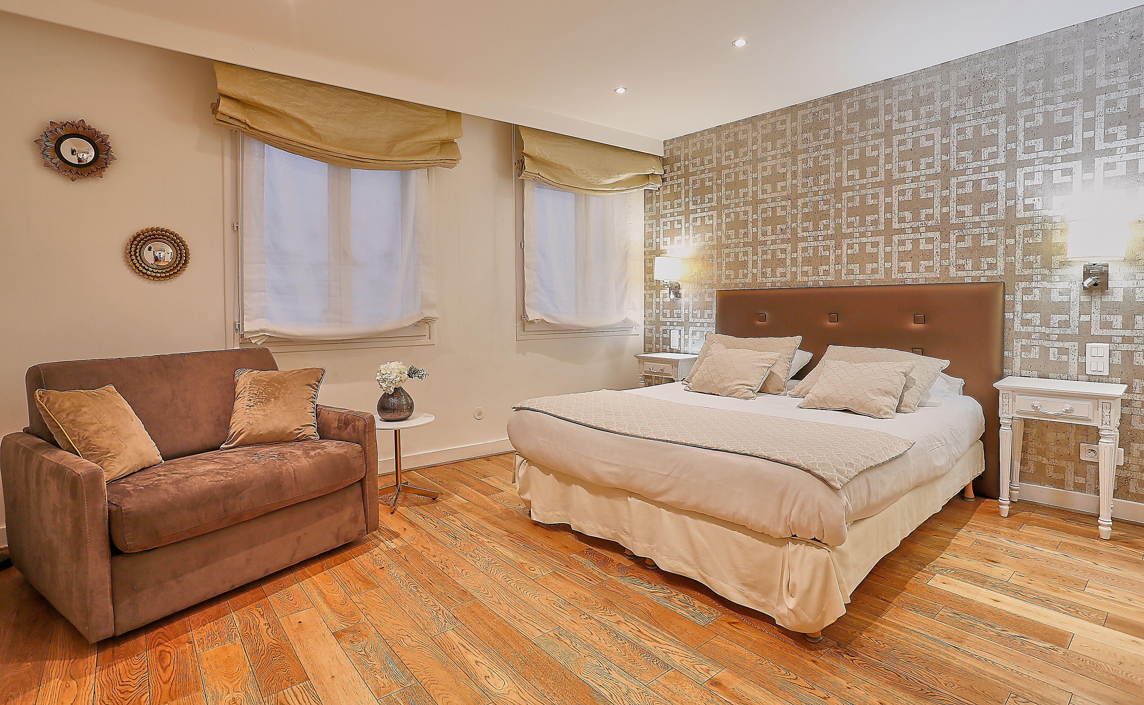 Un dormitorio con una cama grande, un sofá marrón y dos ventanas con cortinas.